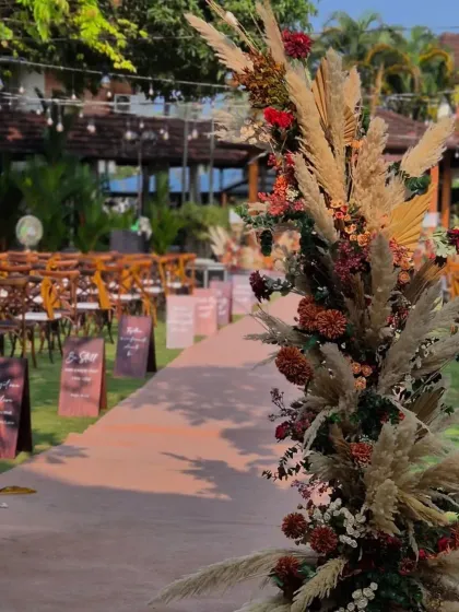 A close-up of the aisle entrance decor. The arrangement combines fluffy pampas grass with deep red and orange florals, establishing the rustic and warm color palette for the entire event.