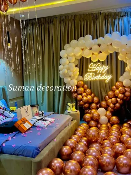 A romantic birthday surprise set up in a bedroom. This features a heart-shaped balloon arch in white and chrome gold, a neon sign, and balloons covering the floor.