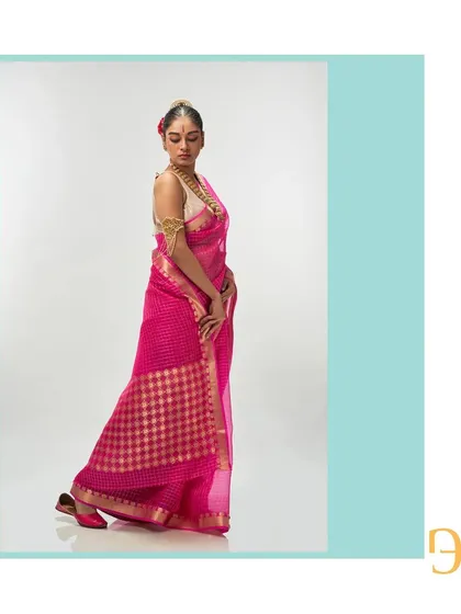 The side profile of the vivid cerise saree shows its elegant drape and the rich texture of the handwoven organza.