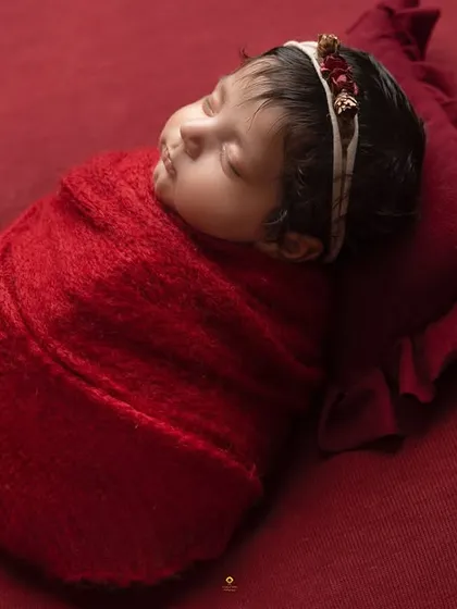 A side-profile of a baby wrapped in red, resting on a matching pillow. This angle is perfect for capturing the delicate curve of their cheek and lips.