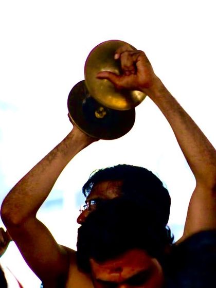 An artistic shot of Kalavadhyam Rohit, his arms raised high, striking the Ilathalam at the peak of the Melam's energy.