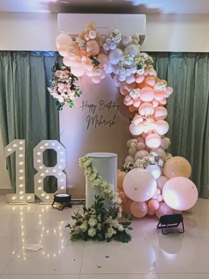 An elegant and modern setup for an 18th birthday celebration. This design features a soft pastel balloon arch with fresh floral accents, a personalized backdrop, and large marquee numbers, creating a chic and memorable photo corner.