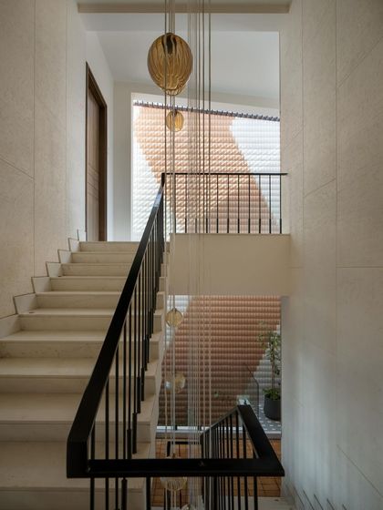 A symphony of light and texture. This staircase features a brick jali wall and delicate hanging lights that add a subtle rhythm, illuminating the path with warmth and grace.