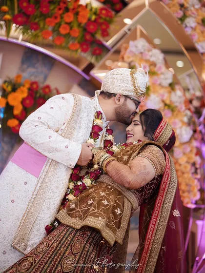 A joyful moment during the Varmala ceremony, with the groom leaning his bride back for a kiss on the forehead.