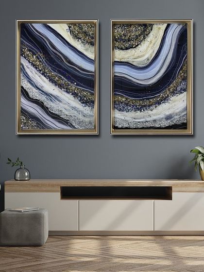 A beautiful set of two resin art paintings in deep blue, white, and gold. The wave-like patterns are filled with glittering crystals, perfect for creating a sophisticated and cohesive look above a console.