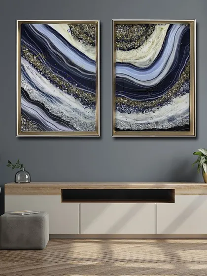 A beautiful set of two resin art paintings in deep blue, white, and gold. The wave-like patterns are filled with glittering crystals, perfect for creating a sophisticated and cohesive look above a console.