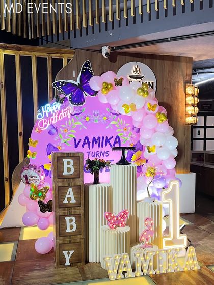 A side view of the purple butterfly first birthday theme, highlighting the 'BABY' blocks and the layered arrangement of the backdrop, balloons, and pedestals.
