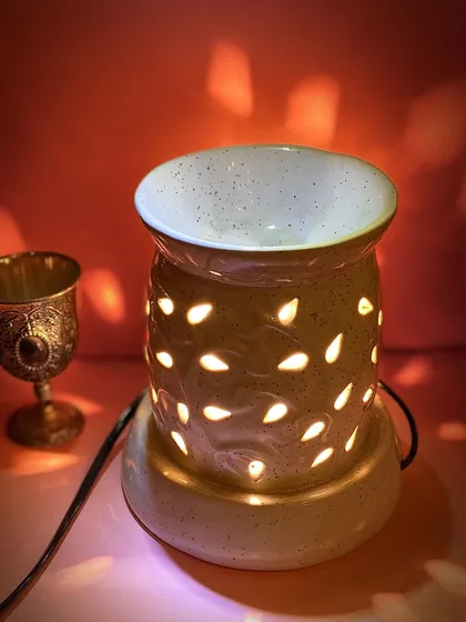 Our electric aroma diffuser creates a warm, inviting glow while filling your room with a relaxing scent. This model features a speckled ceramic finish and teardrop cutouts, casting beautiful light patterns that enhance the calming atmosphere.