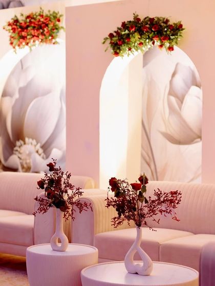 A chic lounge area with minimalist pink sofas and tables, set against a backdrop of modern arches with monochrome floral prints and pops of red flowers.