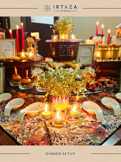 An intimate dinner setup with a beautiful floral-patterned table runner. The warm glow of candles in glass votives creates a cozy and romantic ambiance.