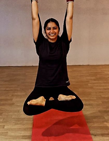 A student joyfully demonstrates a levitating Padmasana (Lotus Pose). This advanced variation builds core strength and balance while showcasing the uplifting feeling of aerial yoga.