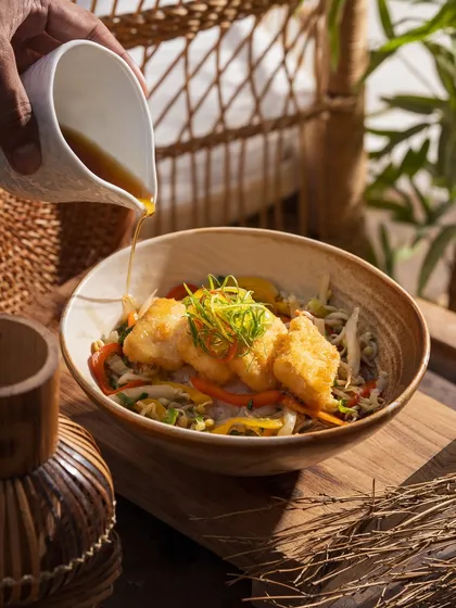 Pouring a savory sauce over a fish and noodle bowl. This action shot adds a dynamic element to the dish.