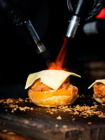 A different angle of the blowtorch in action, highlighting the melting cheese and the intense heat used to create the perfect finish.