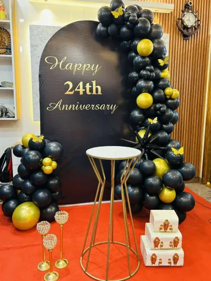 I can create a sophisticated and modern theme for any anniversary. This 24th-anniversary decoration uses a sleek black and gold color palette, with a custom-printed arch backdrop and a cascading balloon garland for a chic and stylish celebration.
