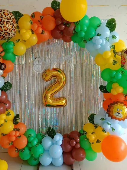 A vibrant jungle-themed second birthday. The circular balloon arrangement is filled with colorful balloons and foil animal heads, set against a shimmering silver tinsel backdrop.