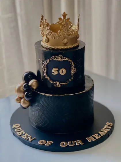 For the "Queen of Our Hearts" on her 50th birthday. This two-tiered black cake features a subtle textured pattern and is topped with an elegant, handcrafted golden crown.