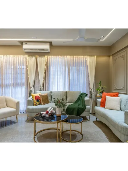 Natural light floods this living room, highlighting the soft textures of the furniture and the subtle details of the wall panels. We believe in creating bright, airy spaces that feel welcoming and serene.