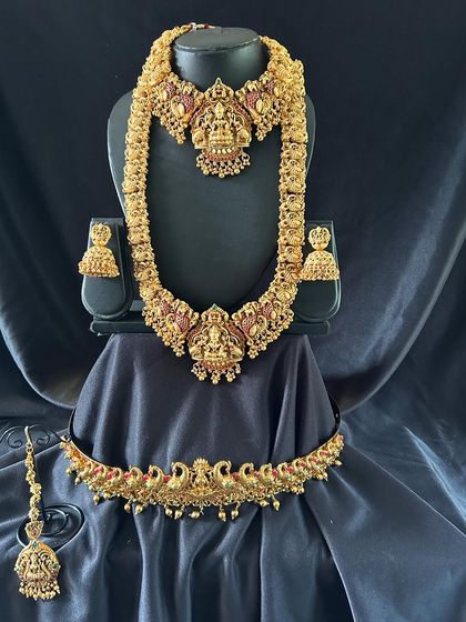 This bridal set features unique peacock and floral motifs with rich kemp stones. The set includes a choker, a long necklace, jhumkas, maang tikka, and a matching peacock vaddanam.