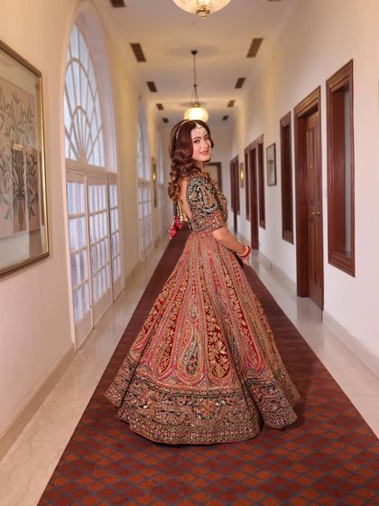 A back view of the bride walking down a corridor, showcasing the grand trail and intricate work on her multi-colored lehenga.