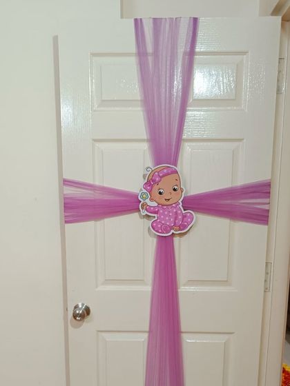 A simple yet sweet door decoration for a baby welcome. The door is wrapped like a gift with purple fabric and a cute baby girl cutout in the center.