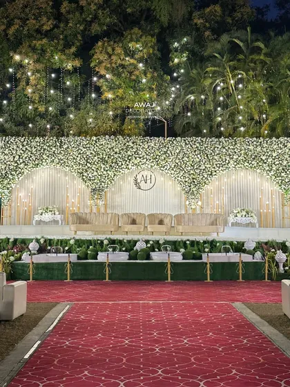 The full view of the white floral stage with a red carpet aisle, contrasting beautifully with the lush green lawn for a classic and grand wedding look.