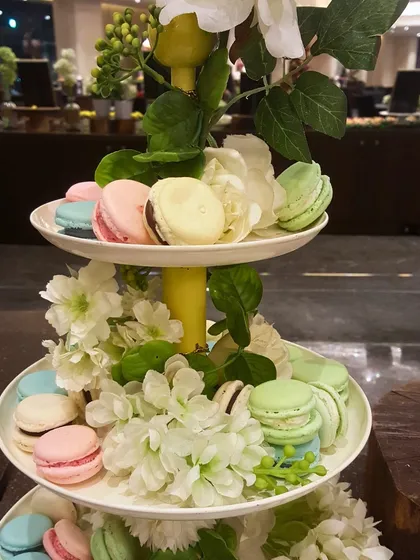 A beautiful three-tiered stand adorned with colourful macarons and fresh flowers. This makes for a stunning centerpiece on any dessert table or high-tea setup.