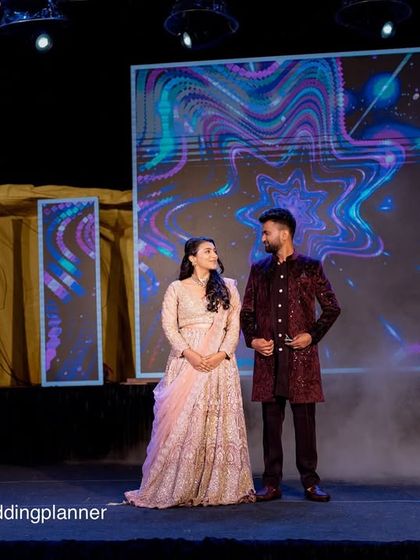 A dramatic stage shot from a Sangeet, with the couple framed by cold pyro sparklers. The large LED screen in the background adds a dynamic, high-energy feel to the event.