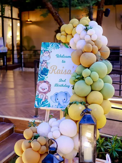 A personalized welcome sign on an easel, decorated with a balloon garland in theme colors, greeted guests at the entrance to Raisa's second birthday party.