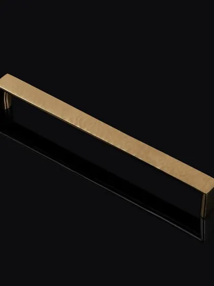 A minimalist shot of a brass-finished rectangular handle on a reflective black surface. This clean, graphic style is ideal for architectural hardware catalogs.
