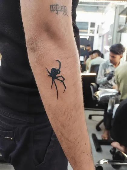 A solid black spider tattoo on the forearm. This bold and graphic design is for those who appreciate the darker side of nature.