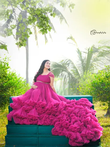 A regal portrait of a mother-to-be in a wine-colored ruffled gown, seated on green steps in our garden.