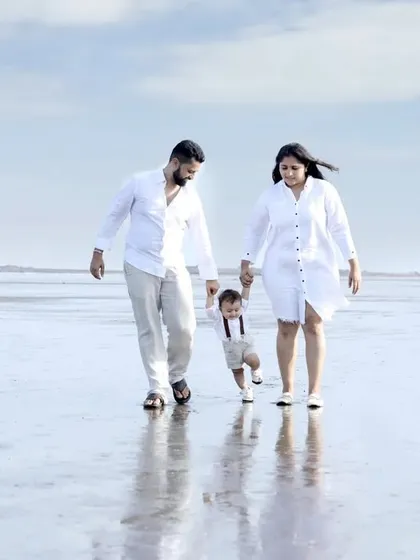A candid shot of parents helping their toddler take his first steps on the wet sand. Our beach photography sessions are perfect for capturing these unscripted, milestone moments for your family.