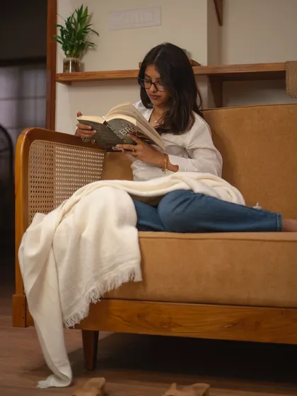 The sofa is a place for comfort and relaxation. Here, a client enjoys a quiet moment on a custom teak and rattan sofa, showcasing its deep, comfortable seat.