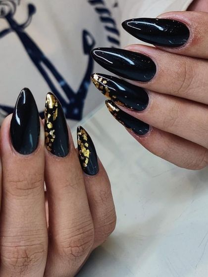 A dramatic and glamorous set of black stiletto nails, with accent nails featuring gold foil flakes for a touch of luxury.