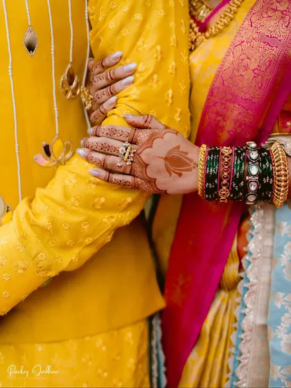 A close-up on the bride's hands, adorned with intricate mehendi and traditional green bangles, as she holds the groom's arm.