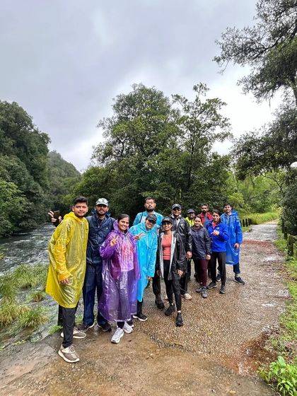 The trekking group posing by the river near the Kurinjal trek base, all geared up in colorful raincoats for the monsoon adventure.