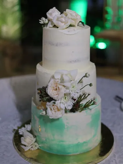 The finished three-tiered wedding cake, standing proud at the reception. The combination of semi-naked layers, watercolour buttercream, and fresh flowers creates a rustic yet elegant look.