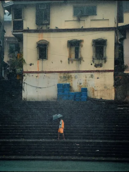 A solitary figure with an umbrella ascends the ancient steps of Banganga. The grainy texture and moody lighting give this photo a timeless, almost historical quality.