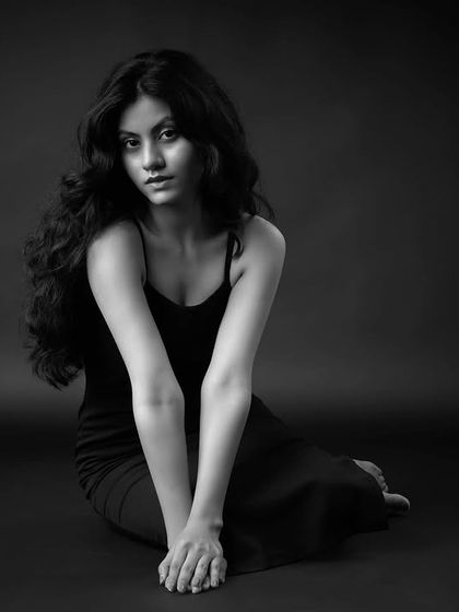 A seated black and white portrait with a moody, contemplative feel. The lighting creates soft shadows, adding depth and emotion to the image.