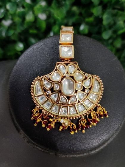 A unique maang tikka with large, rectangular kundan stones and red bead accents.