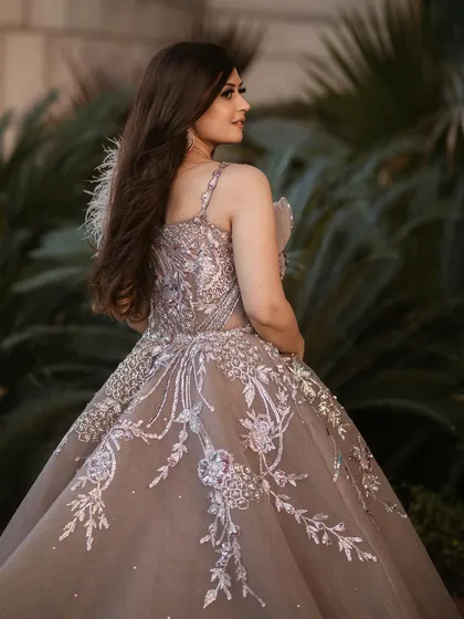 The back and side profile of our rose gold organza gown, highlighting the intricate embroidery that trails down the skirt and the delicate feather accent on the shoulder.