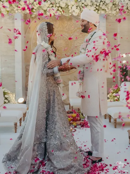 A shower of pink and white petals rains down on the couple, contrasting beautifully with the all-white decor of the mandap.