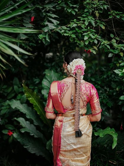 A view of the bride from behind, showcasing her intricate hairstyle and the beautiful design of her saree blouse against the garden backdrop.