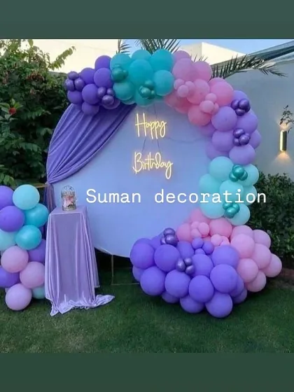 An outdoor garden party setup with a purple, teal, and pink balloon garland on a white circular backdrop.
