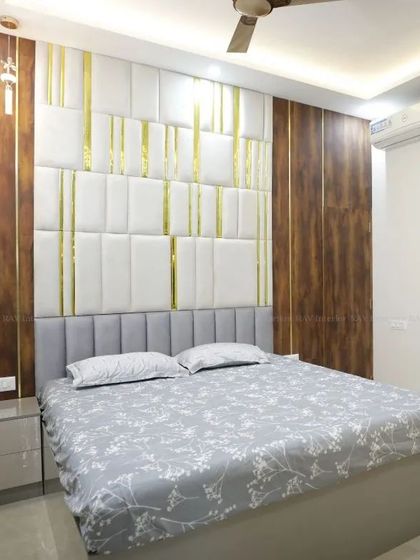 A bedroom with a luxurious feel, featuring a white padded headboard with gold inlays and a comfortable grey bed.