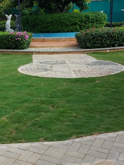 A formal garden area in a public space, featuring a circular paved design, a central water feature, and dolphin statues. The space is framed by well-maintained hedges.