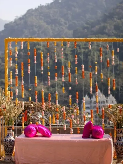 A simple yet beautiful photo booth for a Mehendi or Haldi ceremony. We used a frame with hanging marigold strings against a stunning mountain backdrop, creating the perfect spot for pictures.