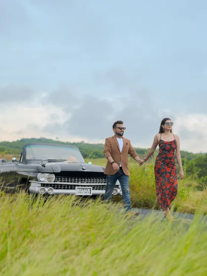 A romantic walking shot with the vintage car in the background. The tall grass and open road give a sense of freedom and adventure.