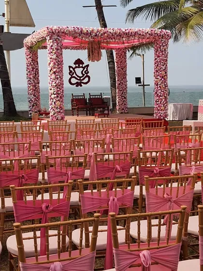 A classic beach wedding setup with a vibrant pink theme. The mandap, adorned with a floral Ganesh motif, is perfectly framed by the sea, with coordinated seating for guests to enjoy the beautiful view.