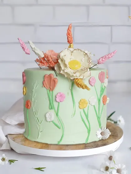 A beautiful pastel green cake with a garden of hand-piped tulips and other spring flowers. This design is fresh, delicate, and full of natural charm.
